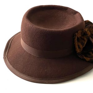 Può includere: Un cappello fedora in feltro marrone con un'ampia tesa e un fiocco con stampa leopardata su un lato.