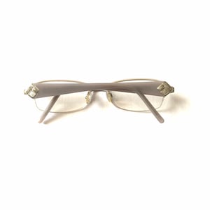 May include: A pair of silver and gold eyeglasses with a rectangular frame. The glasses have a light gray frame and silver accents on the temples.