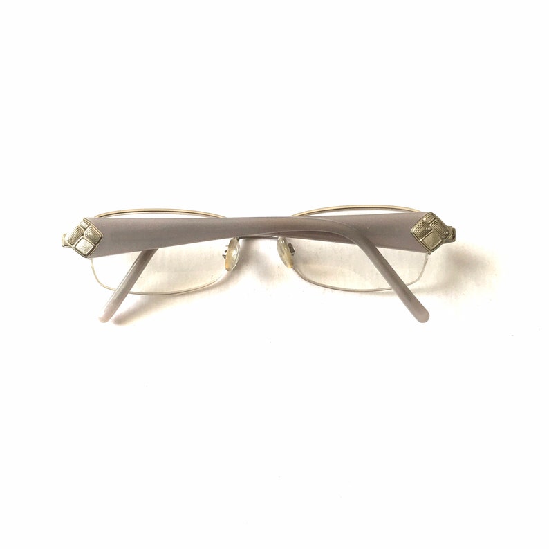 May include: A pair of silver and gold eyeglasses with a rectangular frame. The glasses have a light gray frame and silver accents on the temples.