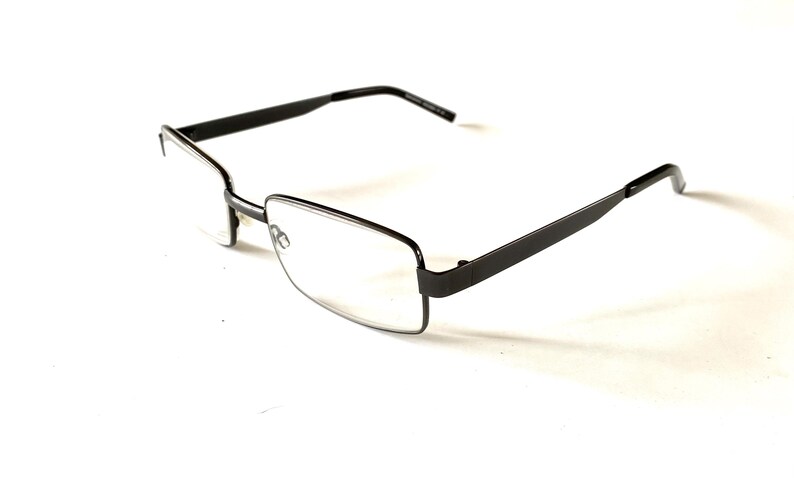 May include: Rectangular eyeglasses with a dark gray metal frame. The lenses are clear, and the arms of the glasses are straight and extend back from the frame. The glasses are set against a white background.