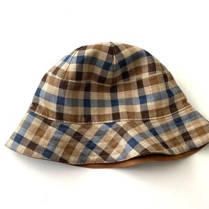 May include: A brown, blue, and tan plaid bucket hat with a brown brim.