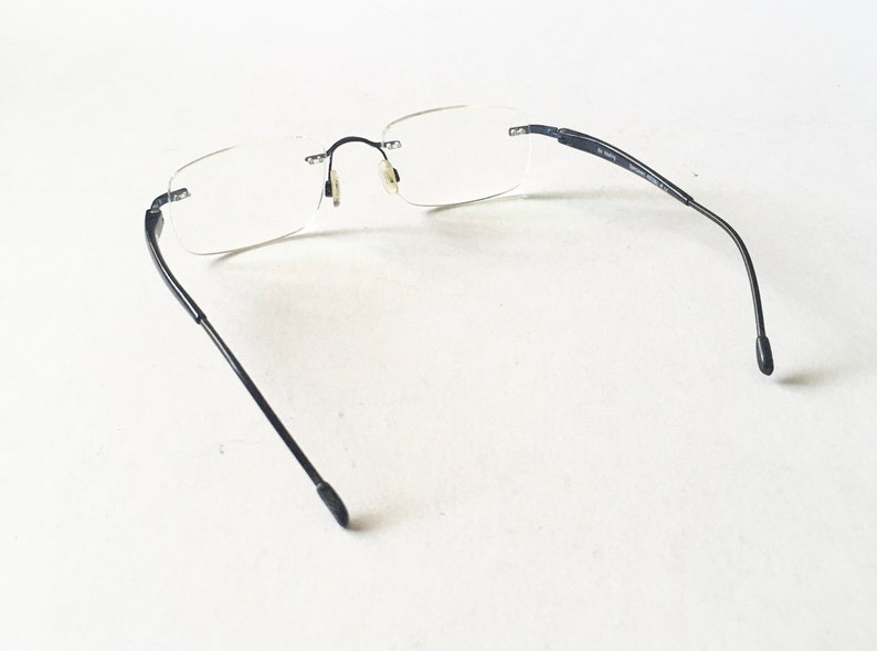 May include: Black rimless glasses with thin arms. The glasses have a rectangular shape and are made of a lightweight material.