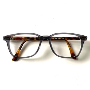 May include: Gray plastic framed eyeglasses with brown tortoise shell arms. The frame has a rectangular shape with rounded edges.
