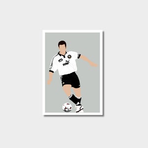 May include: A white and black football shirt with a black Puma logo and a black and yellow team logo. The shirt is being worn by a footballer with a black and white football at their feet.