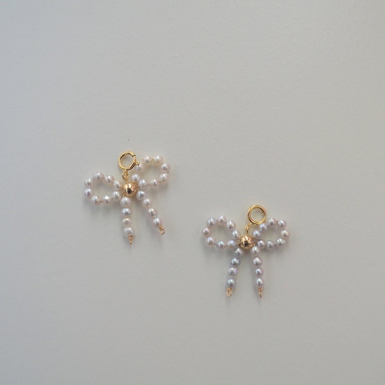 May include: Two gold charm pendants in the shape of bows made of white pearls. Each bow has a gold bead in the center.