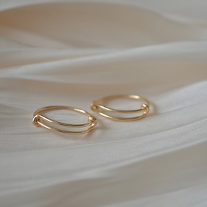 Può includere: Due anelli d'oro con un designo semplice e minimalista. Gli anelli sono realizzati in filo sottile e delicato e hanno una lucentezza discreta.
