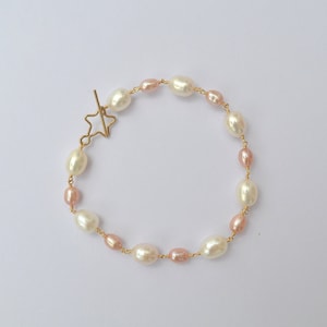 Peut inclure: Un bracelet délicat en perles avec un fermoir étoile en or. Le bracelet présente un mélange de perles blanches et roses.