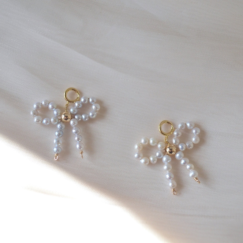 May include: Two gold pearl bow charms with a gold bead in the center. The charms are made of white pearls and are strung on gold wire.