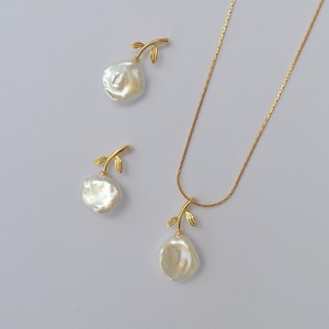 Op de afbeelding: Een gouden ketting met een parel hanger en bladeren accenten. Passende parel oorbellen met bladeren accenten zijn ook inbegrepen.
