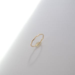 Puede incluir: Un delicado anillo de oro con un diseño ondulado y orgánico. El anillo es delgado y parece estar hecho de metal pulido. El anillo está sobre un fondo blanco, con una sombra proyectada debajo.