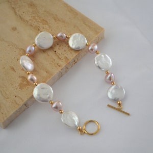 May include: A gold bracelet featuring white and pink pearl beads. The bracelet has a toggle clasp.
