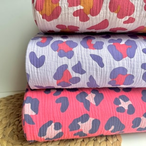 Könnte beinhalten: Drei Rollen Stoff mit Leopardenmuster. Die obere Rolle ist weiß mit rosa und orangefarbenen Flecken. Die mittlere Rolle ist weiß mit lila und rosa Flecken. Die untere Rolle ist rosa mit lila und rosa Flecken.