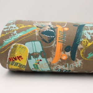 Könnte beinhalten: Brauner Stoff mit einem bunten Druck von Skateboards, Blitzen und dem Wort "Skate" in Rot. Der Stoff hat einen Used-Look.