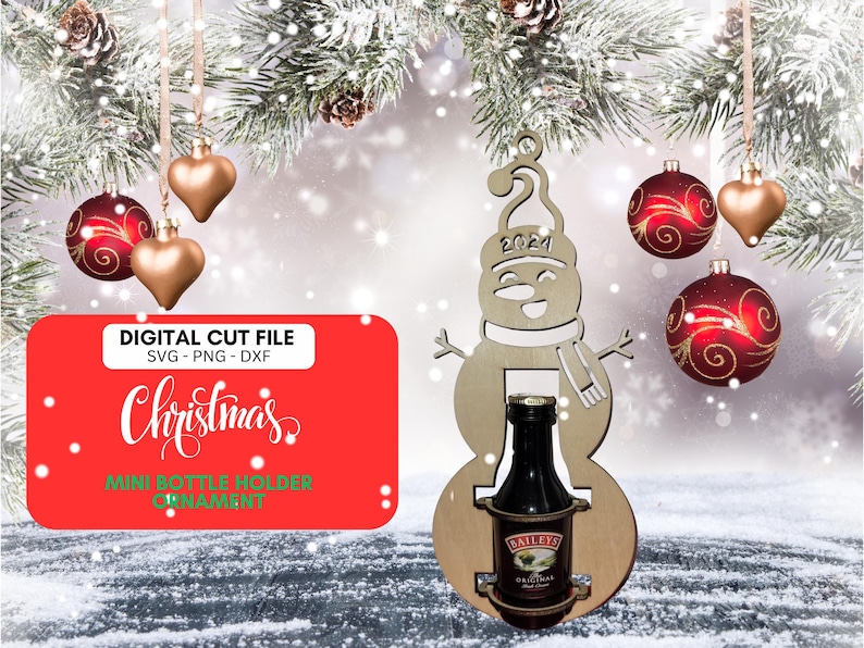May include: Christmas mini bottle holder ornament digital cut file.  SVG, PNG, and DXF files included.  The design features a snowman holding a mini bottle, with '2021' on the hat.  Red and gold Christmas ornaments are in the background.  The file is for creating a Christmas decoration to hold a small bottle of liquor, such as Baileys Irish Cream, shown in the image.