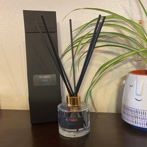 May include: A clear glass diffuser bottle with a gold lid and black diffuser sticks. The bottle has a black label with the text "Handcrafted Candles" and "Savage".