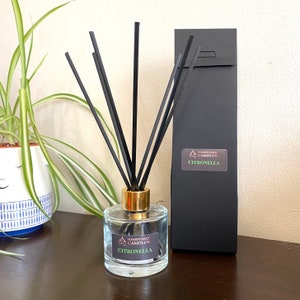May include: A clear glass diffuser bottle with a gold lid and black diffuser sticks. The bottle has a label that reads "Handmade Candles Citronella".