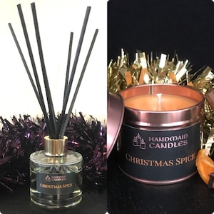 May include: A set of two Christmas-themed home fragrance products. A clear glass diffuser bottle with black reeds and a black and copper candle tin. Both products have a black label with gold lettering that reads "Handmade Candles" and "Christmas Spice".