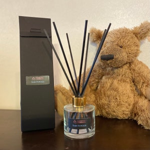 May include: A clear glass diffuser bottle with a gold lid and black diffuser sticks. The bottle has a label that reads "Handmade Candles Baby Powder".