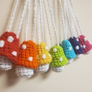 May include: A set of nine crocheted mushroom ornaments in various colors, including red, orange, yellow, green, blue, purple, and pink. Each mushroom has white polka dots and a white stem.