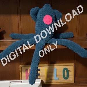 May include: A teal blue crocheted octopus with a pink crocheted flower on its head. The octopus is sitting on a wooden shelf with a sign that says "HELLO" in colourful letters.
