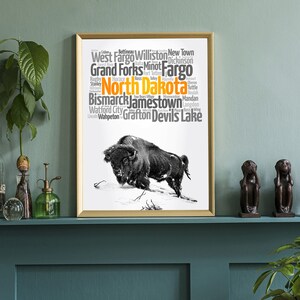 May include: A black and white illustration of a buffalo with a word cloud of cities in North Dakota. The word cloud is in orange and gray text on a white background. The cities listed are: Dickinson, West Fargo, Williston, New Town, Grand Forks, Minot, Fargo, Stanley, Rugby, Horace, Fort Totten, Devils Lake, Bismarck, Jamestown, Mandan, Langdon, Wahpeton, Grafton, and Watford City.