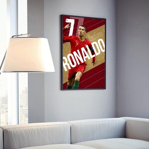 Pu&ograve; includere: Un poster incorniciato con una fotografia di Cristiano Ronaldo in una divisa da calcio rossa e verde, che celebra un gol. Il poster ha uno sfondo rosso e oro con il testo "Cristiano Ronaldo" in bianco.