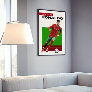 May include: A black framed poster with a white background and a green and red field. The poster features a photo of Cristiano Ronaldo playing soccer with the text "Cristiano Ronaldo" in black.