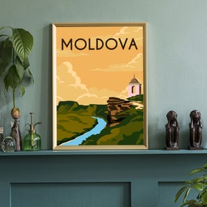May include: A vintage travel poster with a gold frame featuring a landscape scene of a river winding through a valley with a small pink church on a cliff. The poster has the word "MOLDOVA" in bold, yellow letters at the top.