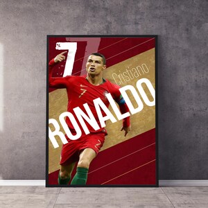Pu&ograve; includere: Un poster con una foto di Cristiano Ronaldo con una maglia da calcio rossa e verde, che celebra un gol. Il poster ha uno sfondo rosso e oro con il testo "Cristiano Ronaldo" in bianco.