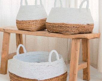 Peut inclure: Trois paniers tissés blancs et bruns avec des poignées, posés sur un banc en bois. Les paniers sont de tailles différentes et sont disposés en rangée.