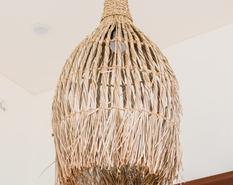 May include: A woven pendant light fixture with a natural straw-like material and a fringe detail. The light fixture is hanging from a black cord.