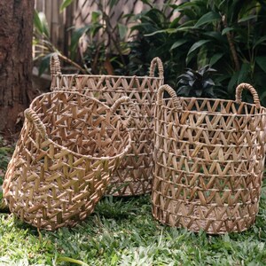 May include: Three woven baskets made of natural materials, with a chevron pattern. The baskets are different sizes and are sitting on a bed of green grass.