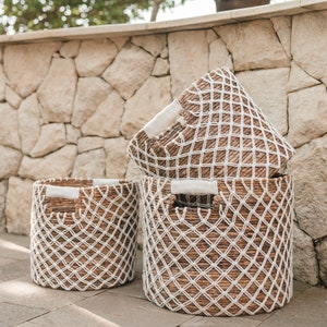 Könnte beinhalten: Drei geflochtene Körbe mit weißen Seil-Akzenten. Die Körbe sind übereinander gestapelt und aus natürlichen Materialien gefertigt. Die Körbe sind hellbraun und haben ein natürliches, rustikales Aussehen.