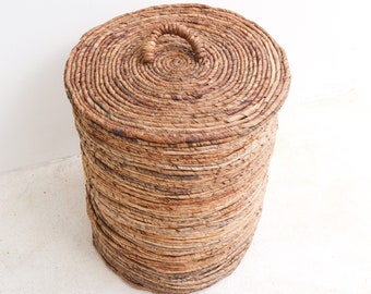 Peut inclure: Un panier de rangement rond en osier avec un couvercle et une poignée. Le panier est fait de matériaux naturels et a une couleur brun clair.
