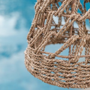 May include: A close-up of a woven lampshade made of natural fibers. The lampshade is a light brown color and has a textured surface. The lampshade is woven in a tight pattern, creating a geometric design.