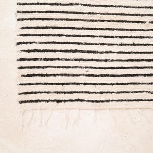 May include: A white rug with black stripes. The rug has a fringe border.