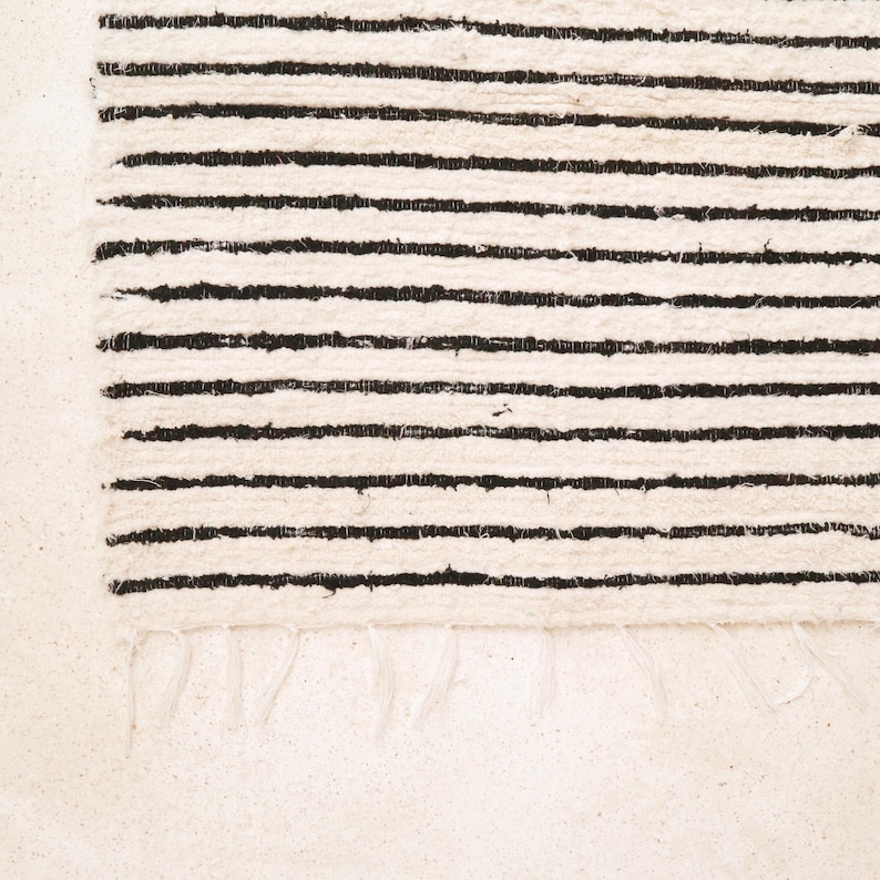 May include: A white rug with black stripes. The rug has a fringe border.