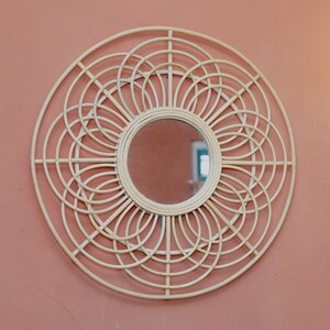 May include: A large, round, white wicker mirror with a circular mirror in the center. The mirror has a decorative design of overlapping circles.