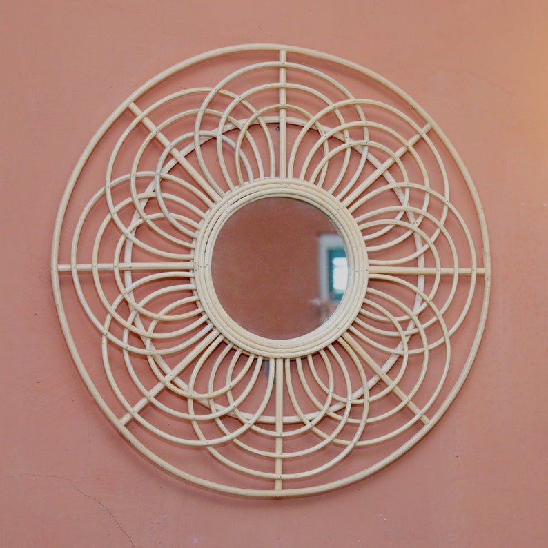 May include: A large, round, white wicker mirror with a circular mirror in the center. The mirror has a decorative design of overlapping circles.