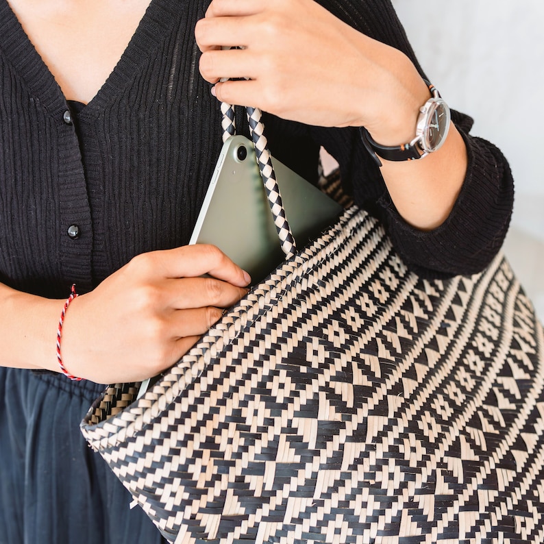 May include: A black and white woven tote bag with a tablet computer tucked inside. The bag has a geometric pattern and is being held by a person wearing a black sweater.