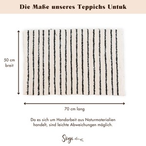 May include: A black and white striped rug with a white background and black stripes. The rug is 70 cm long and 50 cm wide. The text "Die Ma&szlig;e unseres Teppichs Untuk" is at the top of the image. The text "70 cm lang" is below the rug. The text "50 cm breit" is to the left of the rug. The text "Da es sich um Handarbeit aus Naturmaterialien handelt, sind leichte Abweichungen m&ouml;glich." is below the rug. The text "Soeji" is at the bottom of the image.