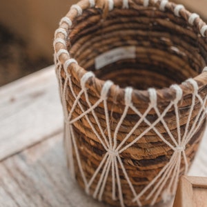 May include: A brown woven basket with white rope accents. The basket has a round shape and is made of natural materials.