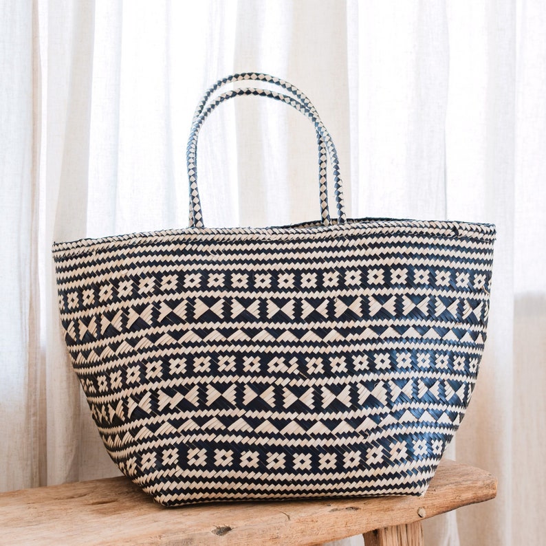 May include: A large, woven tote bag with a black and white geometric pattern. The bag has two handles and is made of a natural material.