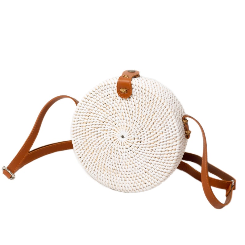 May include: White round woven straw bag with a brown leather strap and a brass buckle.