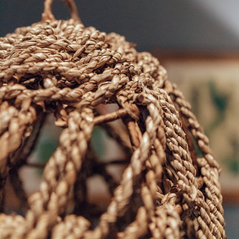 May include: A close-up of a woven basket made of natural fibers. The basket is brown and has a circular shape. The weave is tight and intricate, creating a textured surface. The basket is partially obscured by a blurry background.