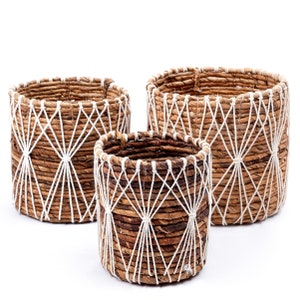May include: Set of three brown woven baskets with white rope accents. The baskets are of different sizes and have a geometric pattern.
