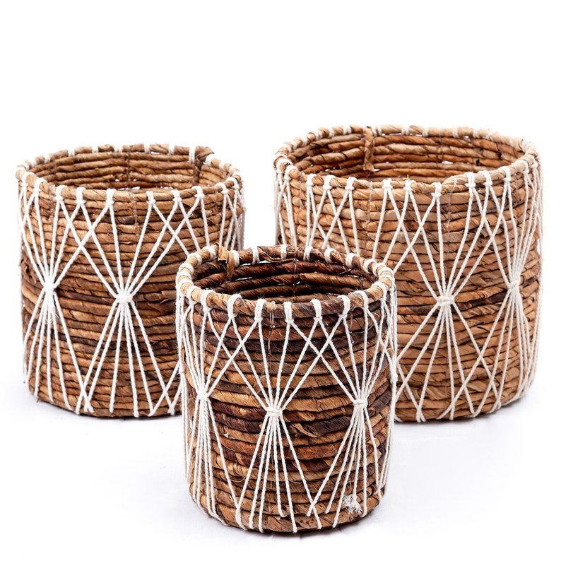 May include: Set of three brown woven baskets with white rope accents. The baskets are of different sizes and have a geometric pattern.