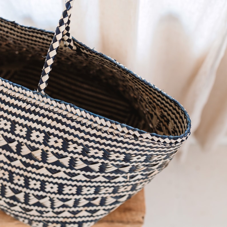 May include: A black and white woven tote bag with a geometric pattern. The bag has a wide, flat base and a single handle.