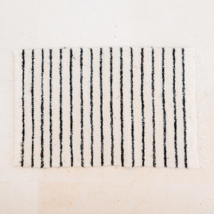 May include: A white and black striped rug with a woven texture. The rug has a frayed edge.