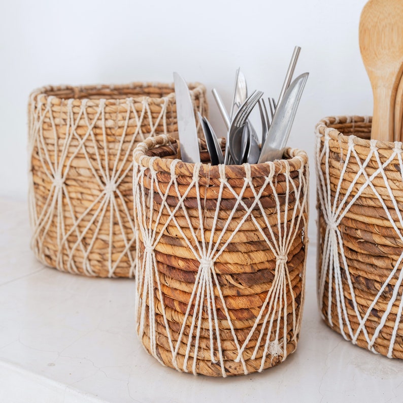 May include: Three woven baskets with a natural brown and white color scheme. The baskets are made of natural materials and have a geometric pattern. The middle basket is filled with silverware.